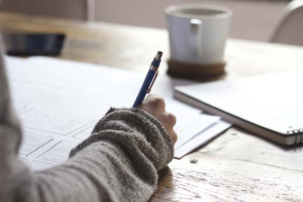 person writing at a desk with a coffee cup and notebooks for editorial standard