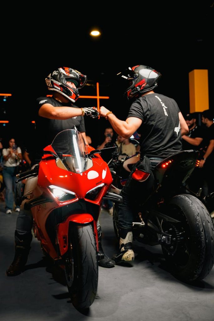 Two bikers on motorcycles exchange a fist bump in an urban setting at night.