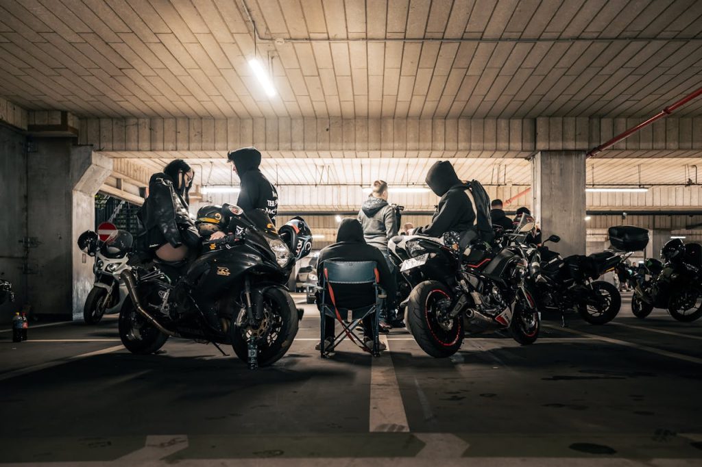 A group of people with motorcycles gather in an industrial parking garage, creating an urban subculture vibe. e MC Authority Distribution Framework™