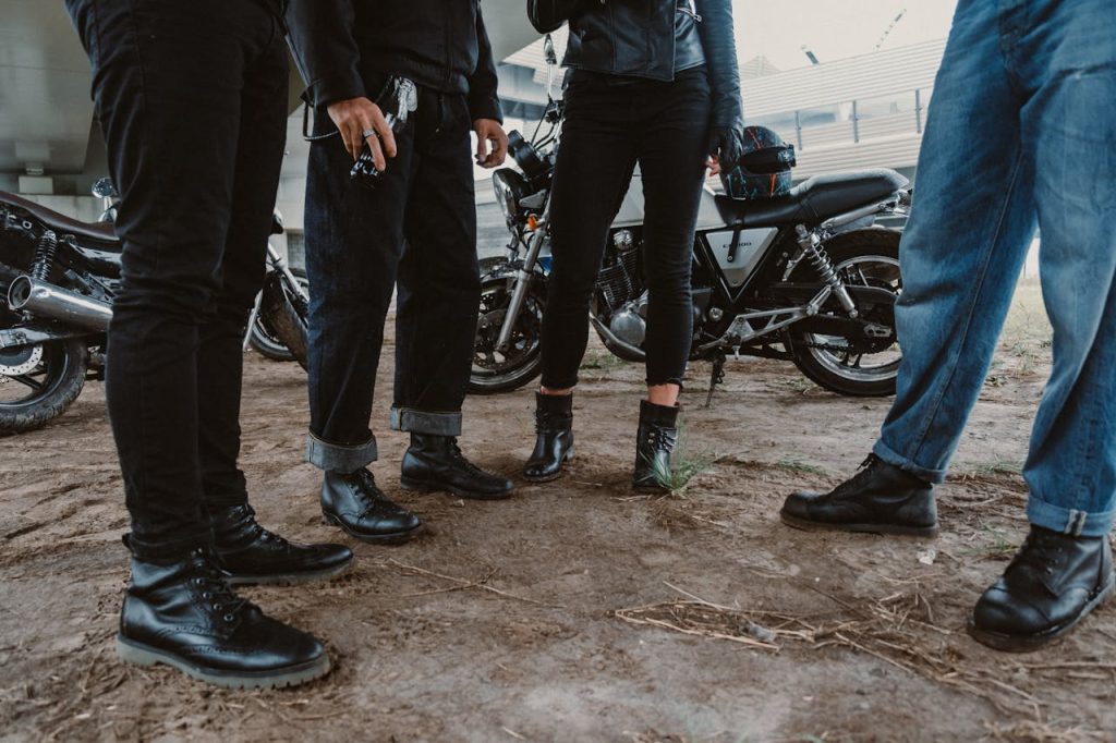 A group of bikers in jeans and leather standing together with motorcycles outdoors. for foundational frame work